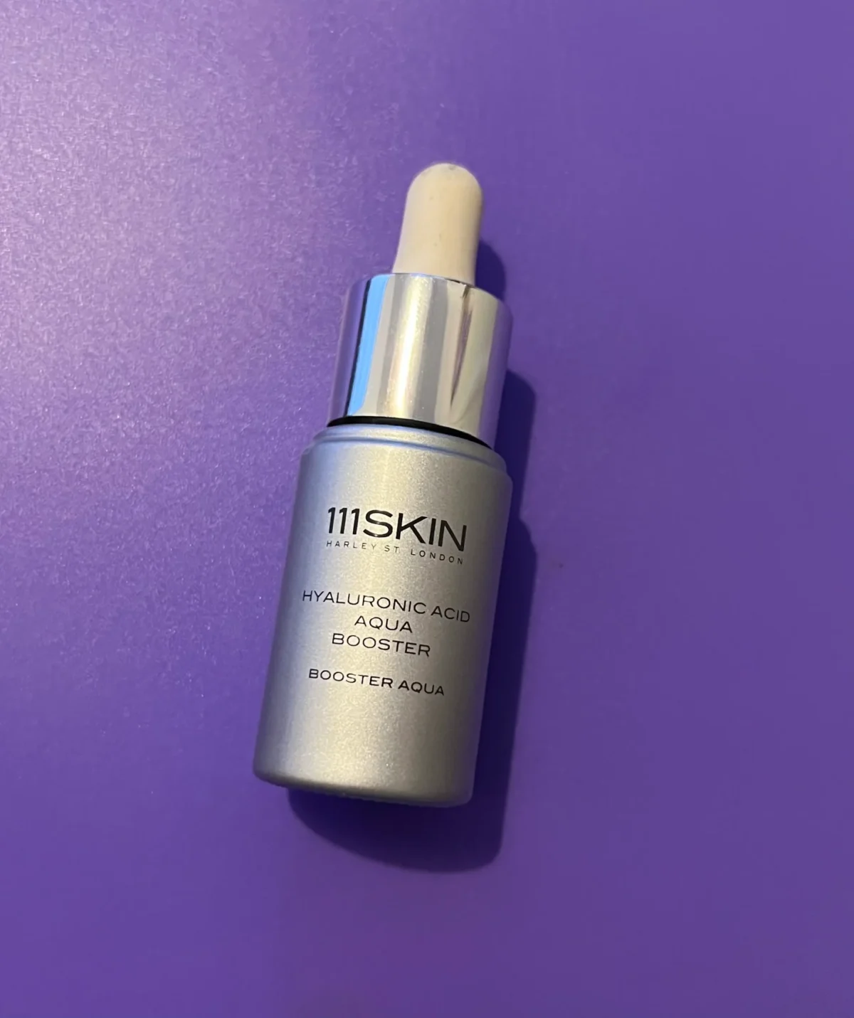 111SKIN Hyaluronic Acid Aqua Booster bottle photographed on a purple background