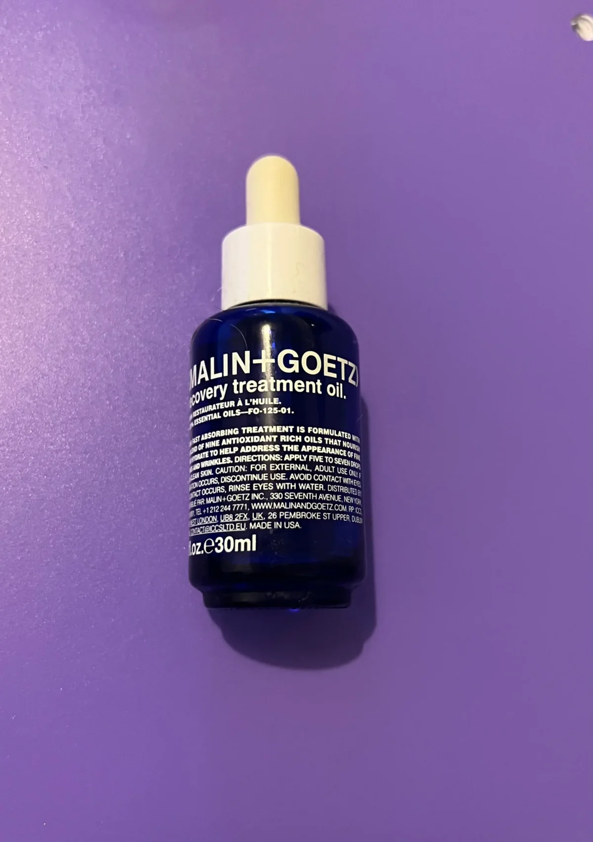MALIN+GOETZ Recovery Treatment Oil bottle photographed on a purple background