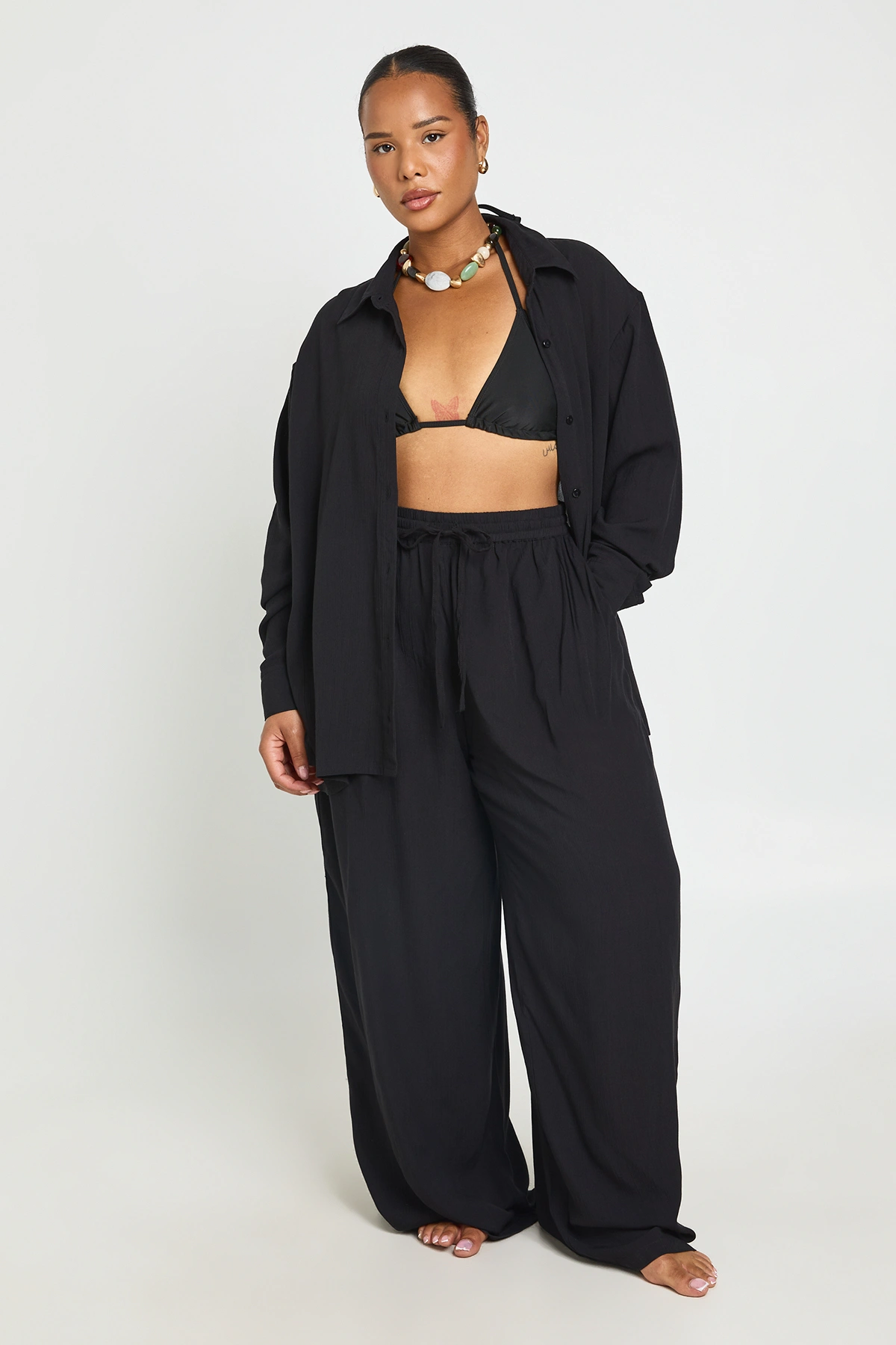 Model wearing the black Boohoo plus-size cheesecloth shirt and trouser beach co-ord