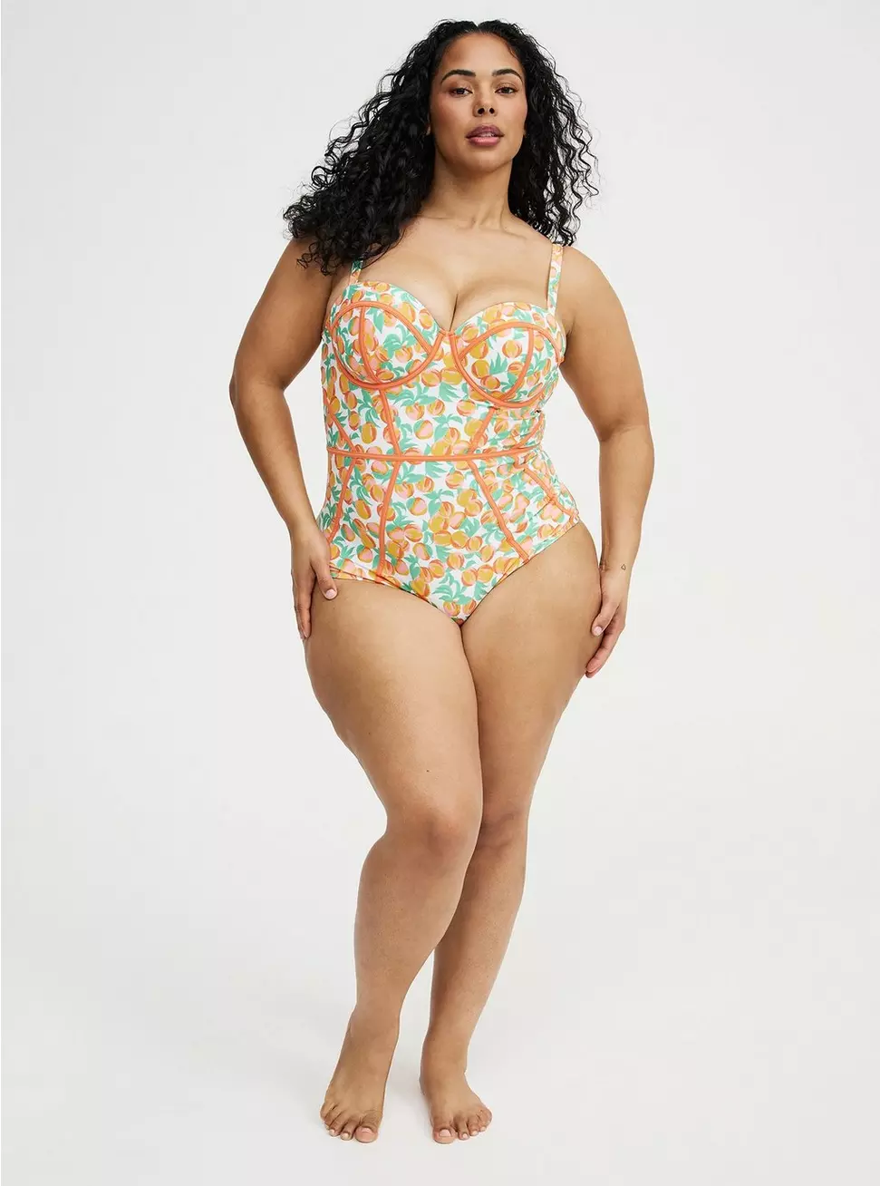 Model wearing the Torrid fruit-print Slim Fix underwire one-piece swimsuit with orange piping