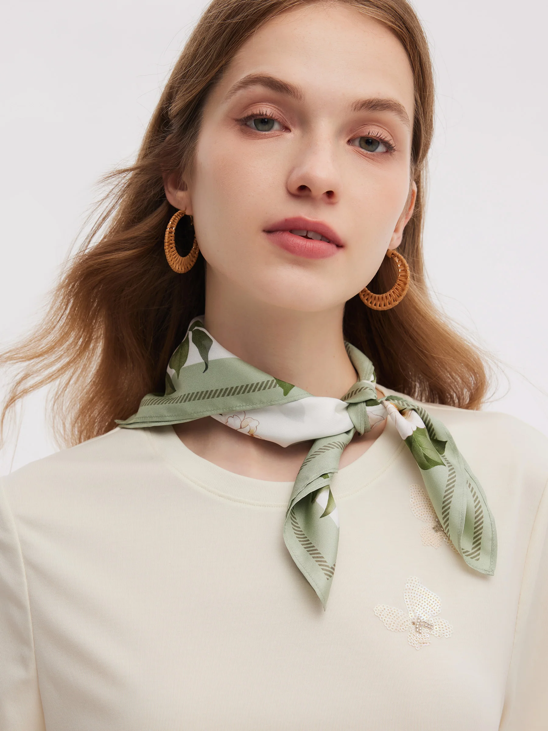Woman wearing a pale green and cream floral scarf tied at the neck.