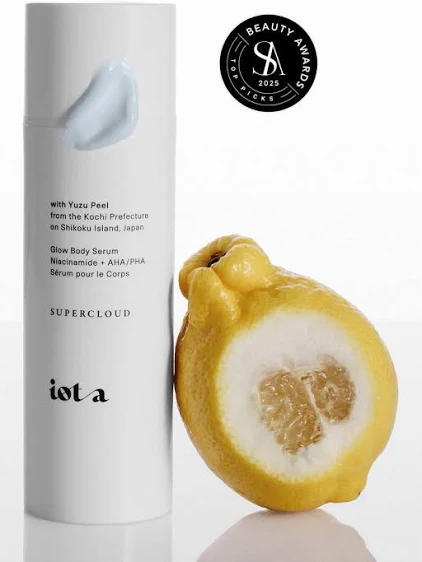 White iota Supercloud Body Serum bottle beside a sliced fruit.