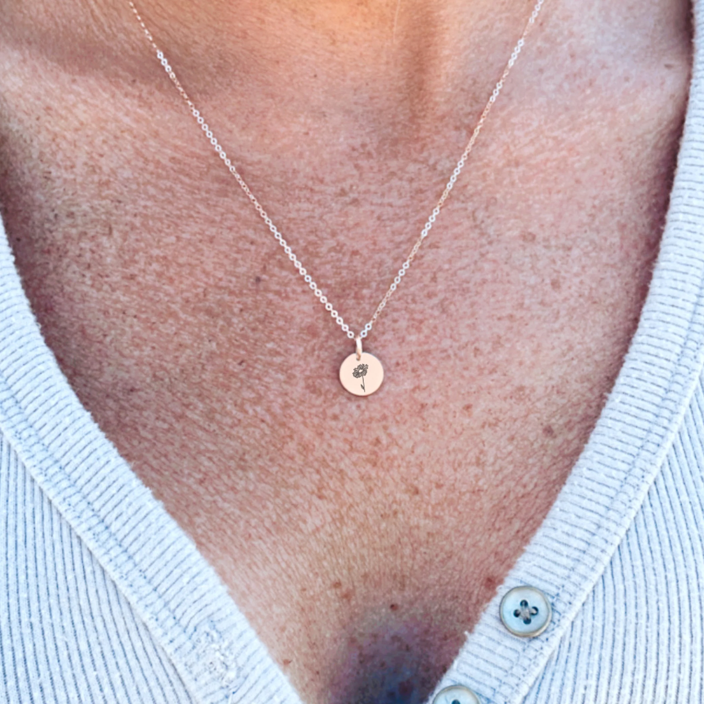 Small birth-flower disc necklace worn on a fine chain.