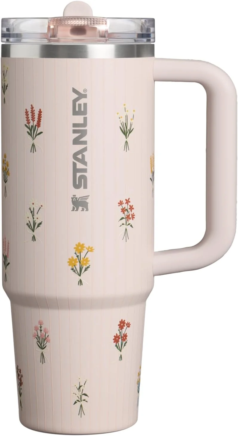 Pale pink Stanley handled tumbler with small floral illustrations and a flip-straw lid.